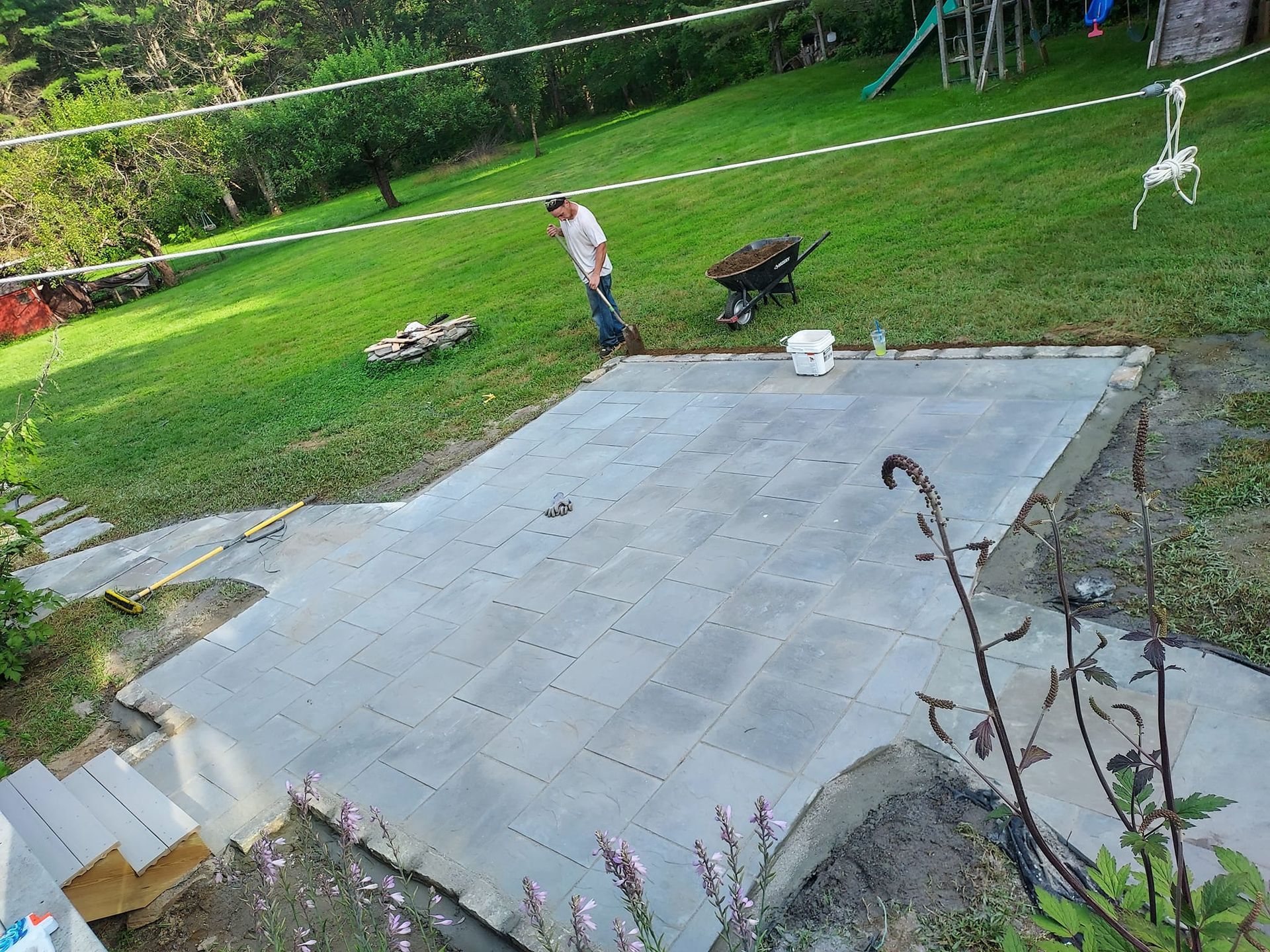 Man working on a gray concrete patio in a grassy backyard.