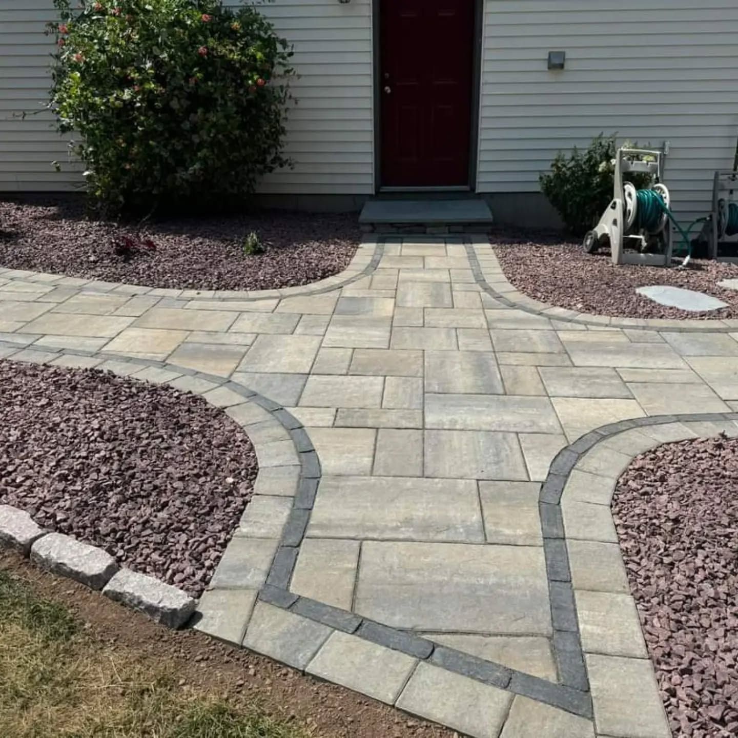 Stone walkway splitting into two paths, surrounded by red gravel and a green lawn.