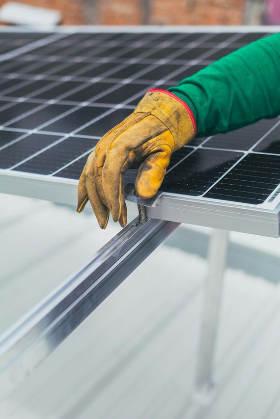 Hand in work glove touches solar panel frame.
