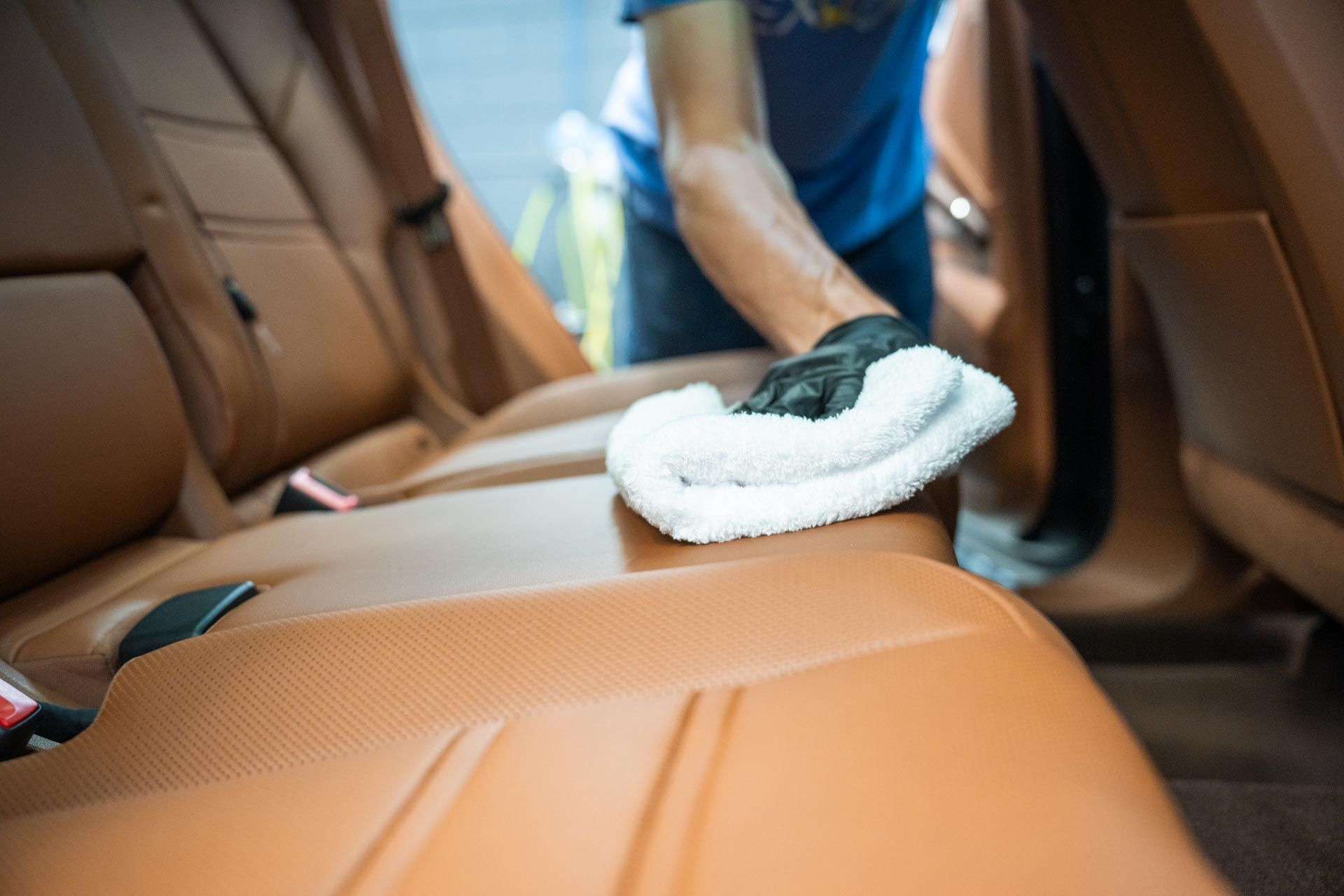 Person cleaning brown leather car seat with white cloth.