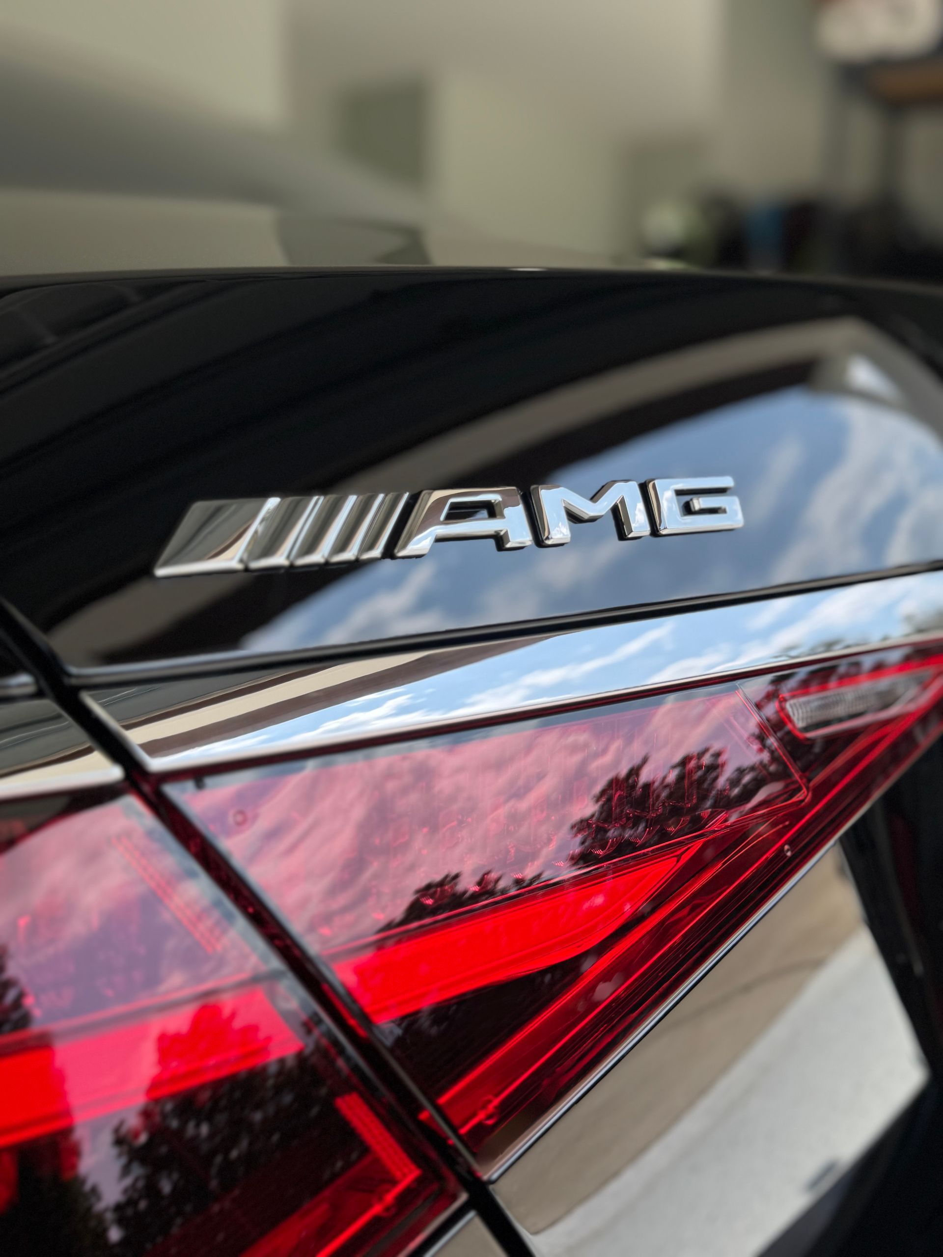 Close-up of a black car's rear, featuring a silver AMG emblem above a red taillight.
