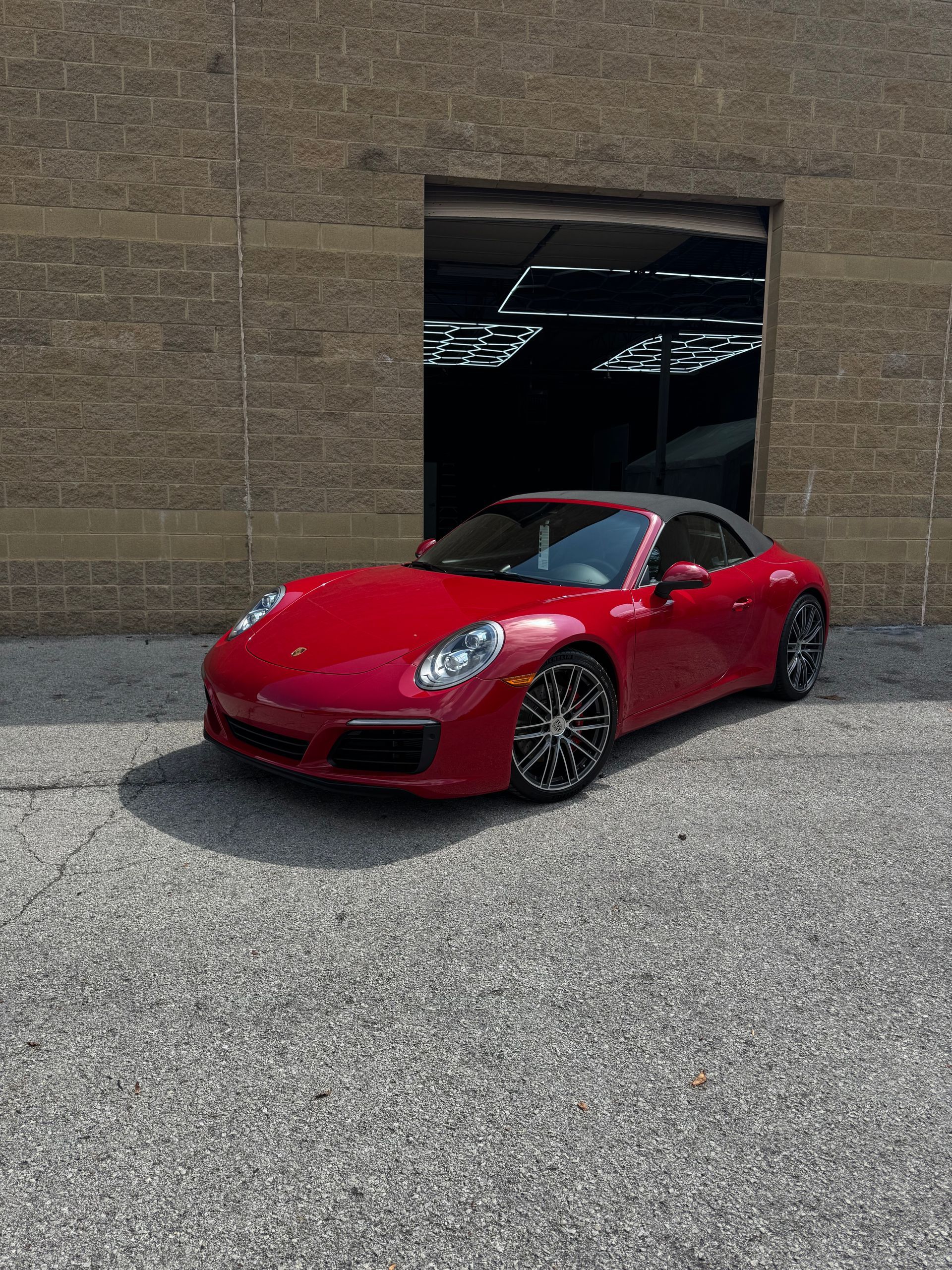 Red convertible sports car parked in front of a brick building with a dark doorway.
