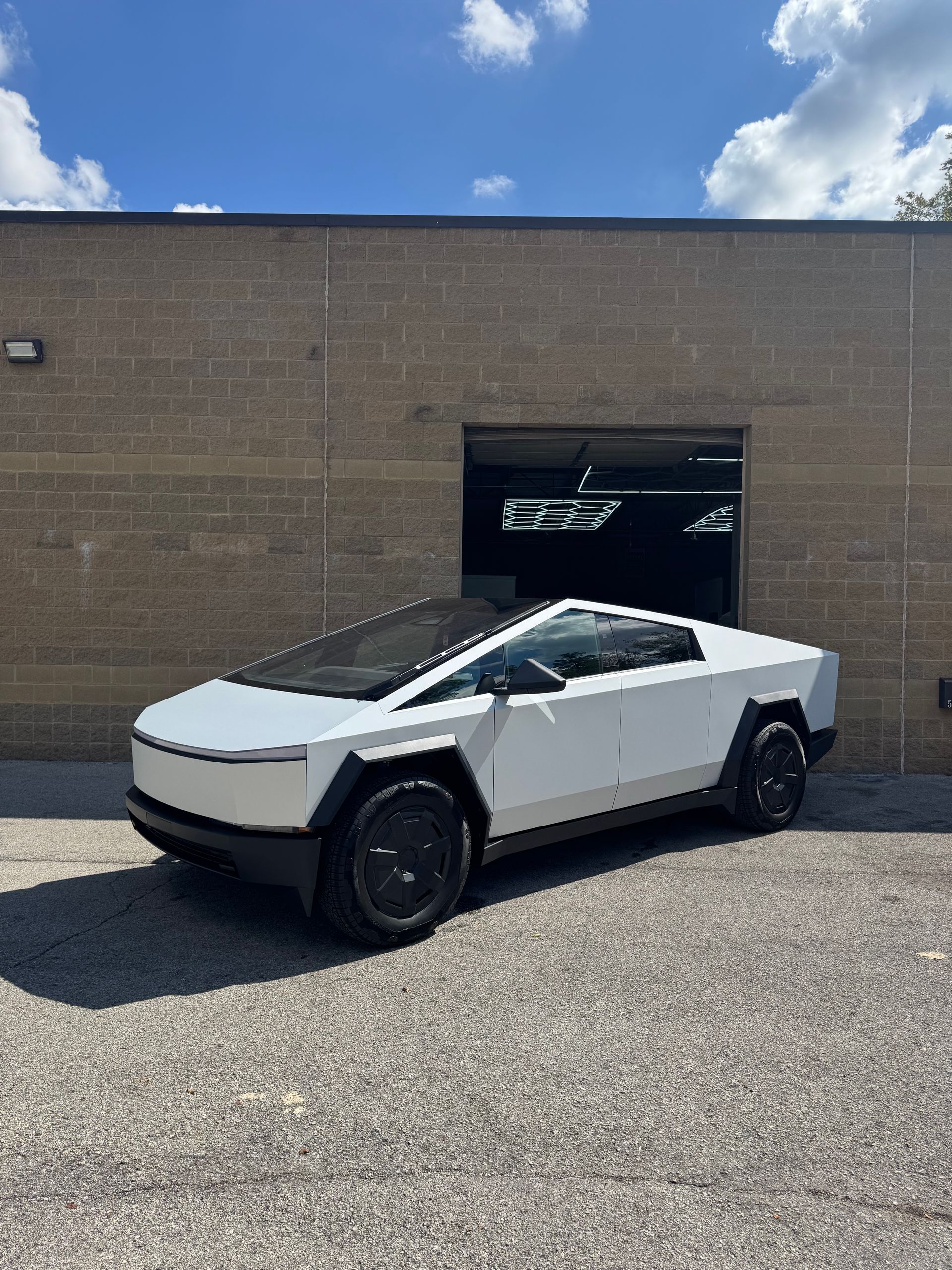 White Tesla Cybertruck parked in front of a gray brick building, under a blue sky.