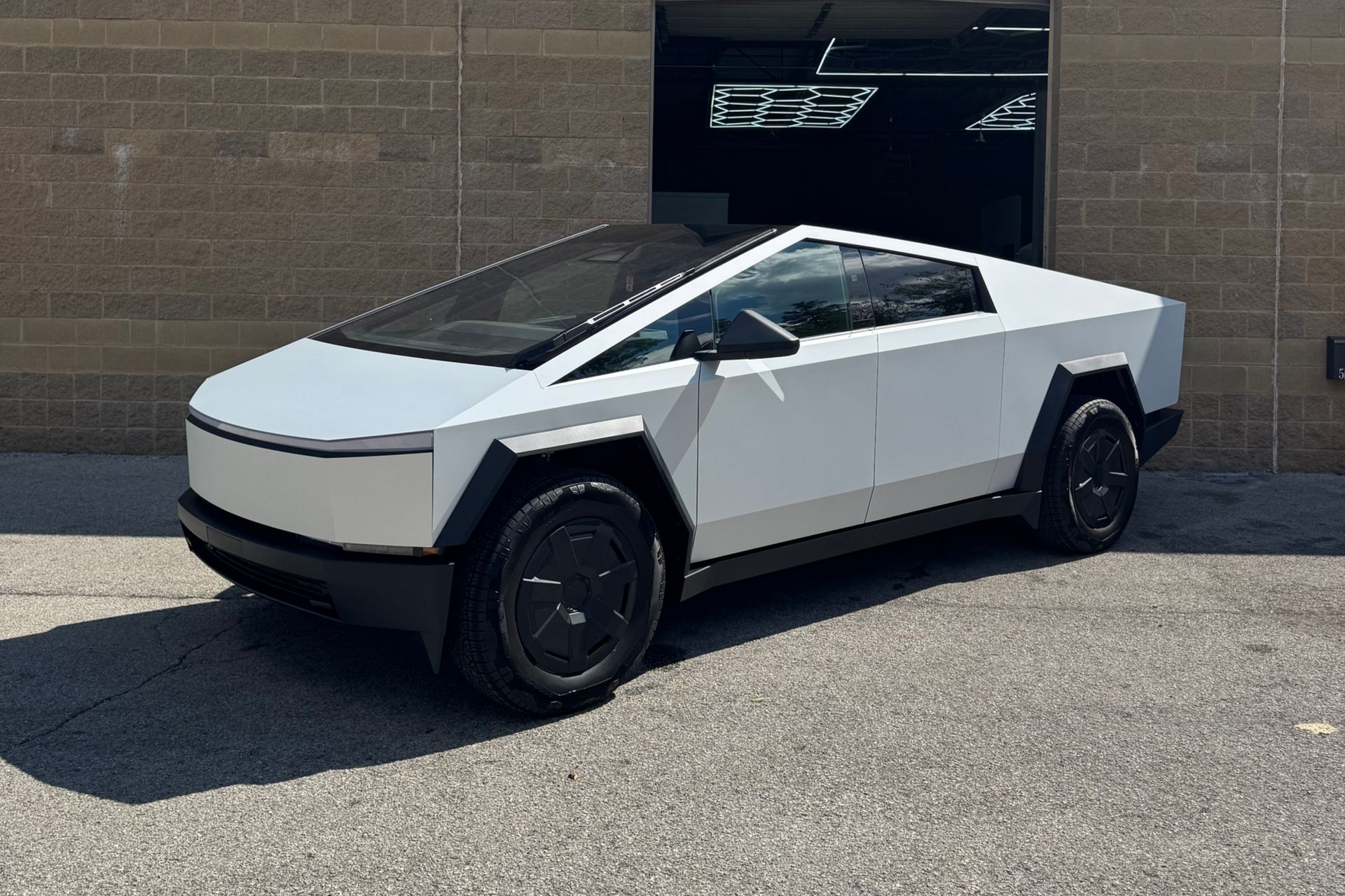 White Tesla Cybertruck parked in front of a gray brick building, under a blue sky.
