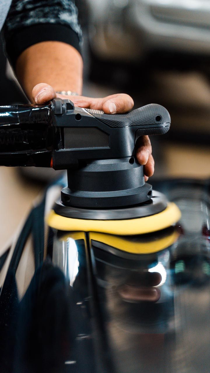 Person using a black and yellow polishing machine on a black car panel.