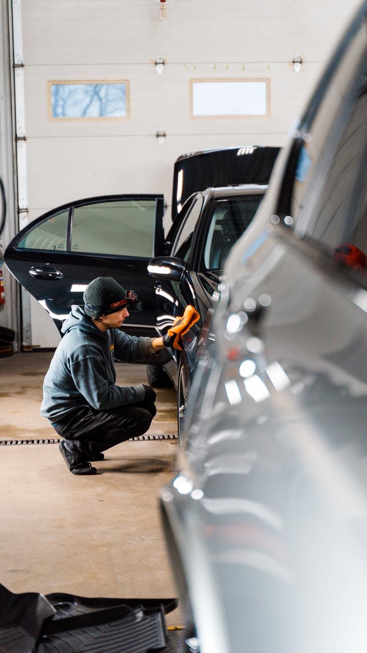 Person wiping down a black car in a garage.