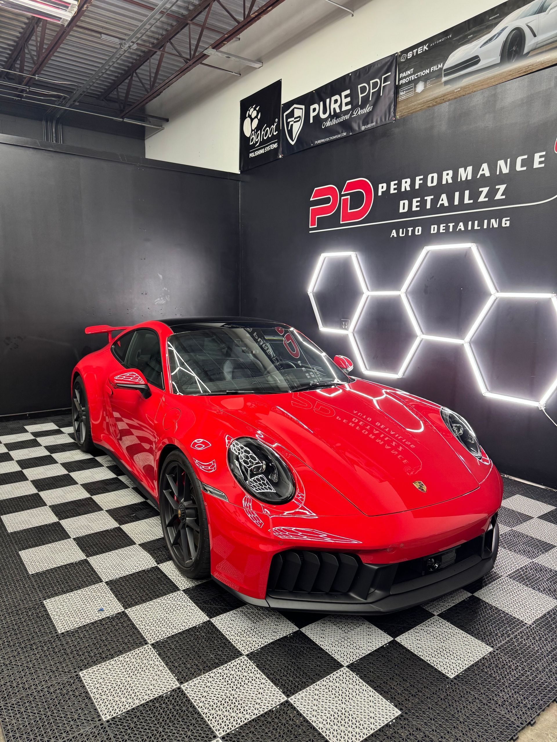 Red Porsche 911 parked in a detailing shop with a black and white checkered floor, under neon lights.