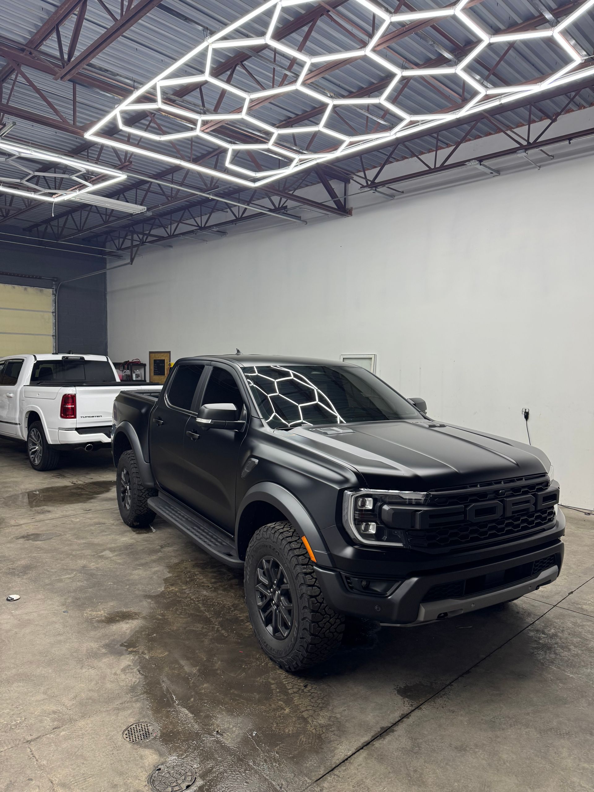 Black Ford pickup truck inside a well-lit auto shop, another white truck in the background.
