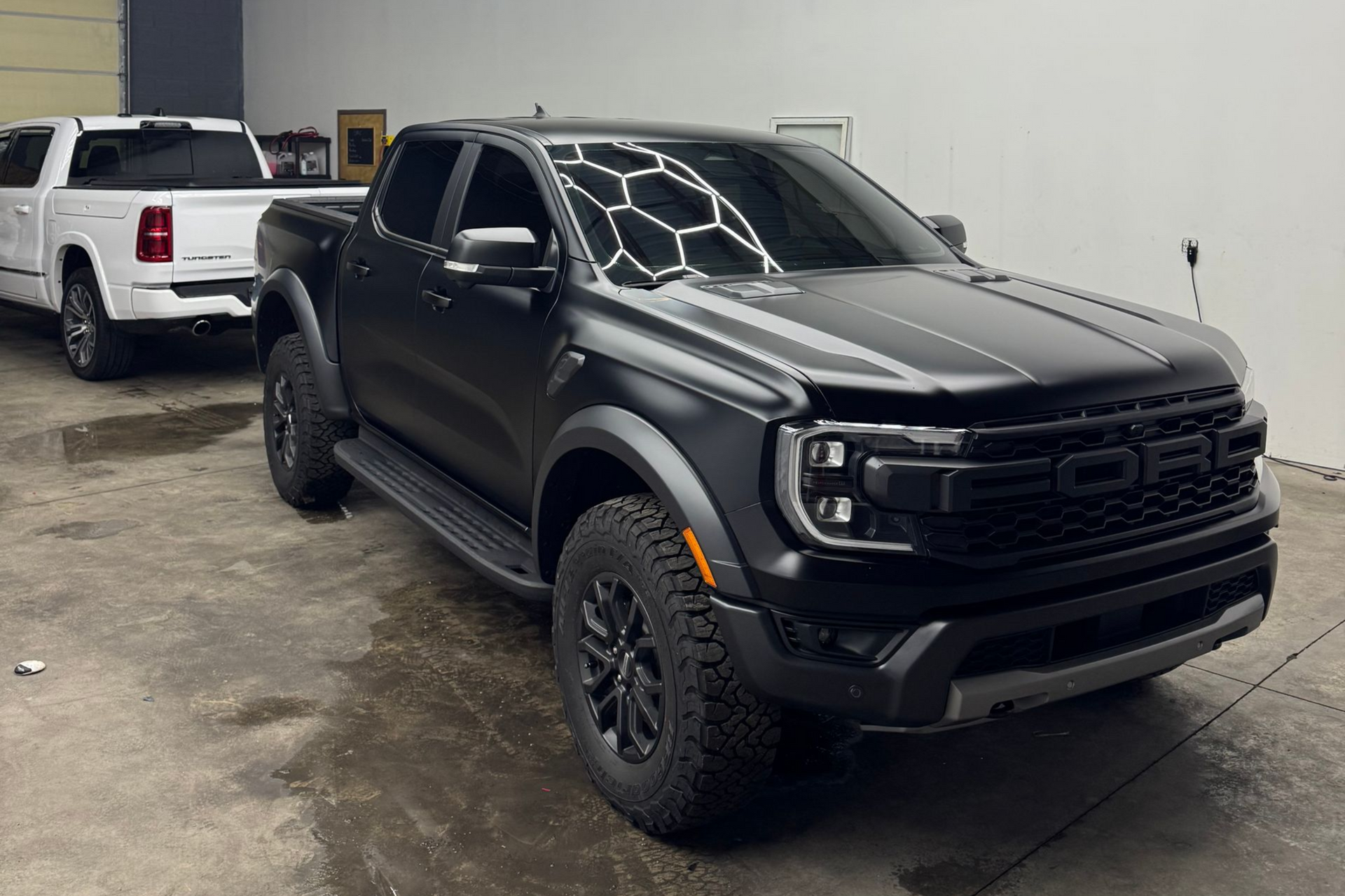 Black Ford pickup truck inside a well-lit auto shop, with a white truck in the background.