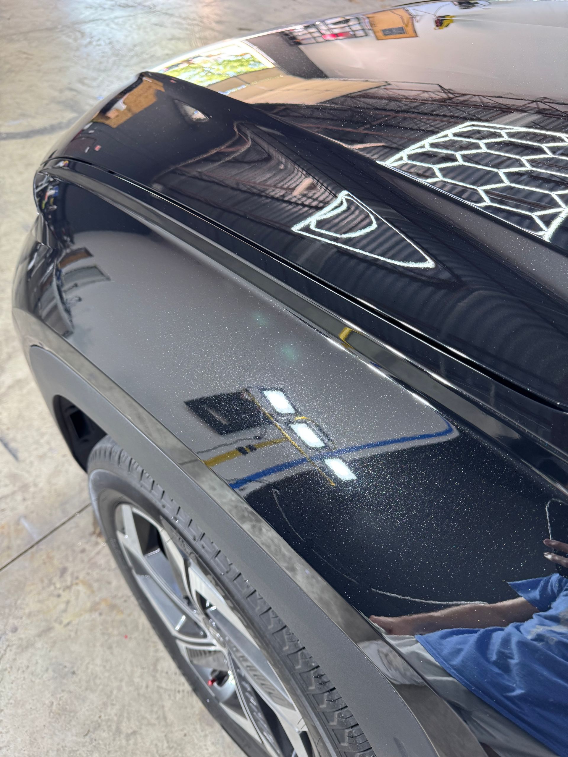 Black car fender with tire and visible imperfections reflecting light.