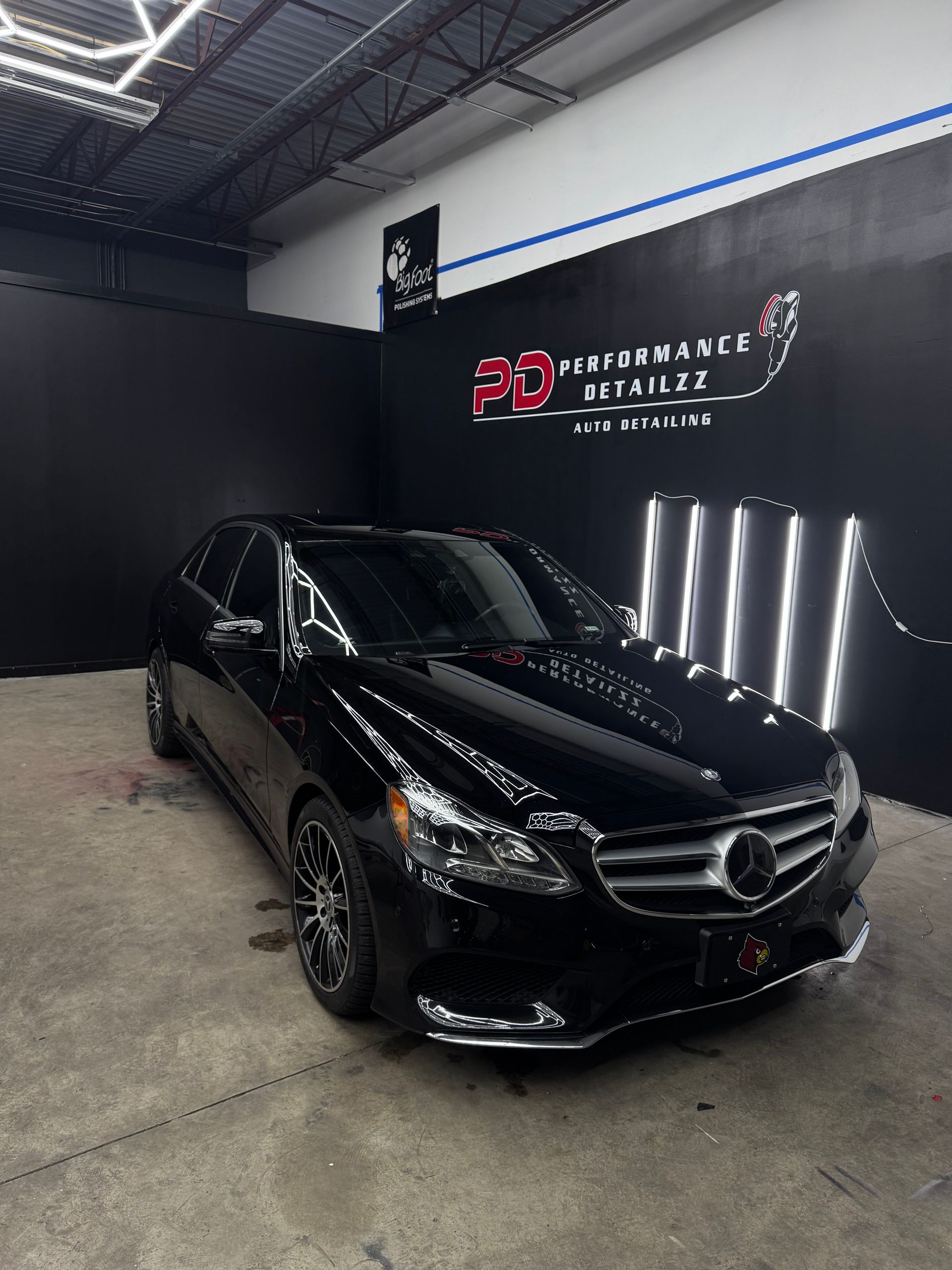 Black Mercedes sedan in a detailing shop, with the shop's logo on the wall.