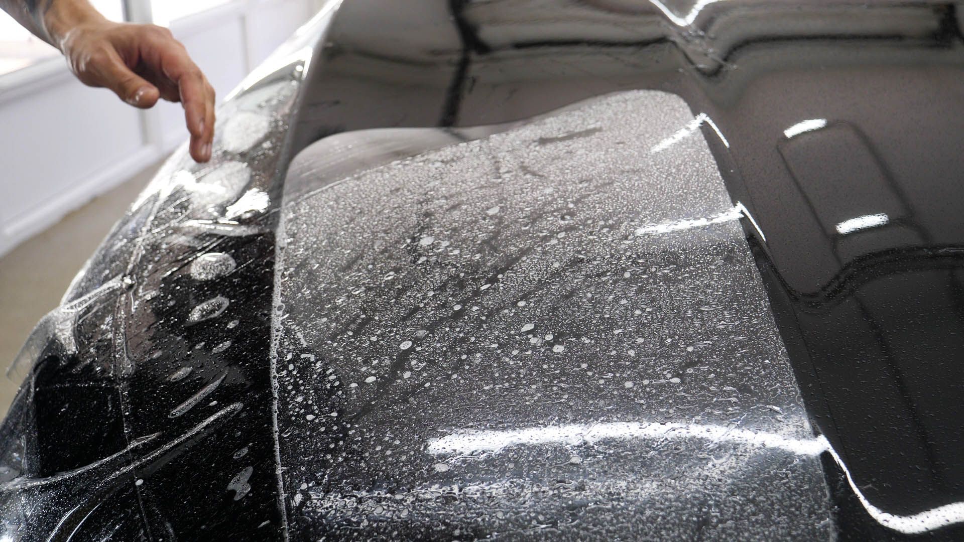 A person's finger pointing at clear film being applied to a black car surface, showing bubbles.