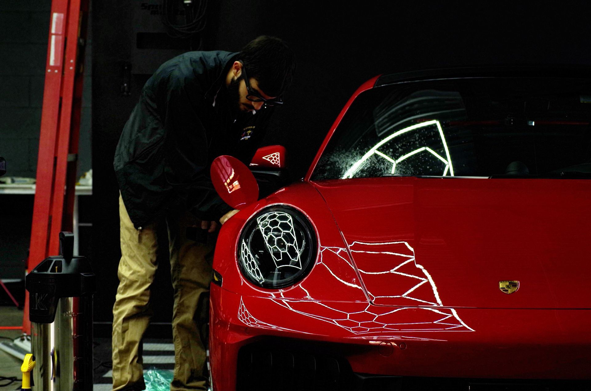 Man examining a red Porsche in a garage.