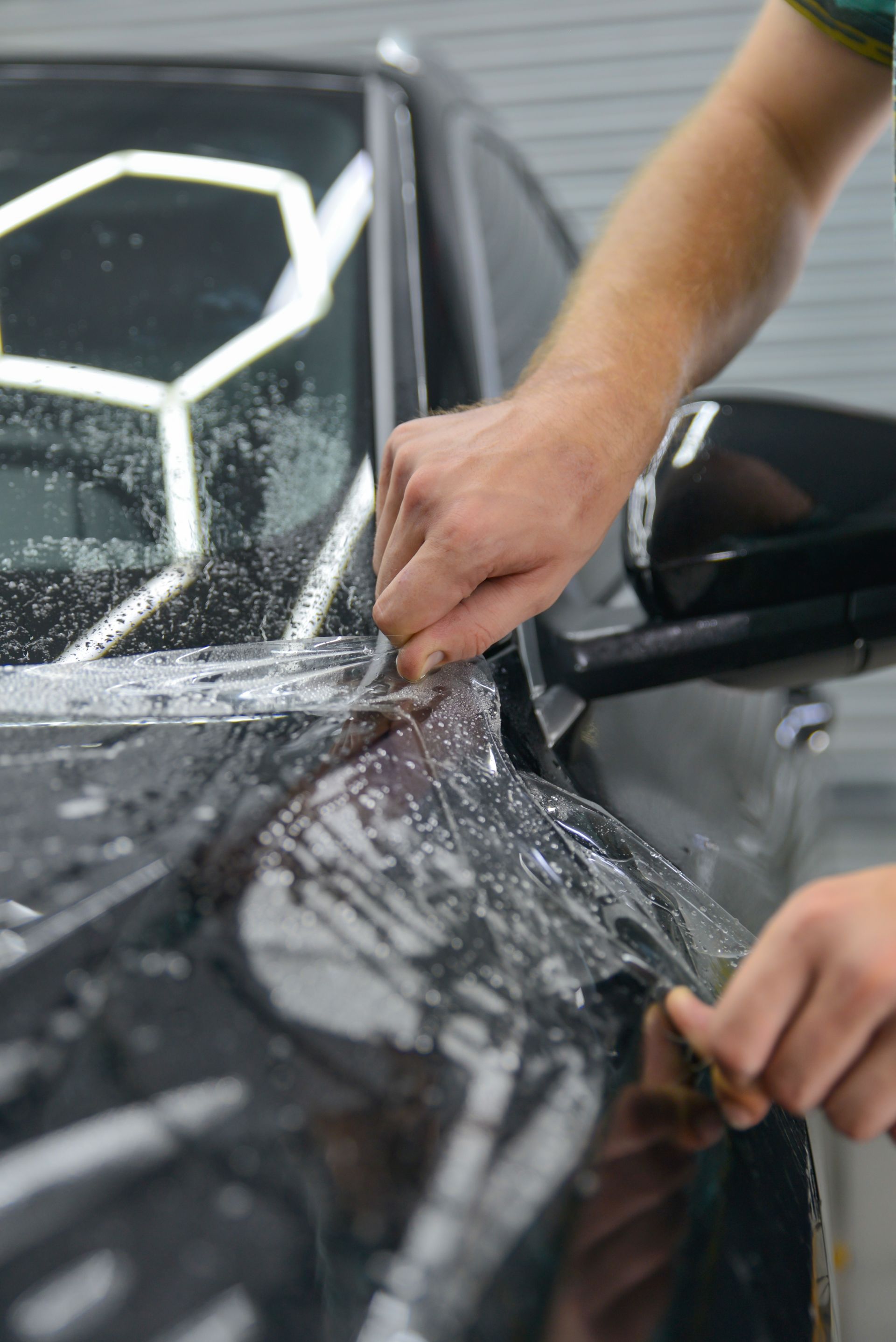 Clear film being applied to a car's headlight, with water droplets visible.