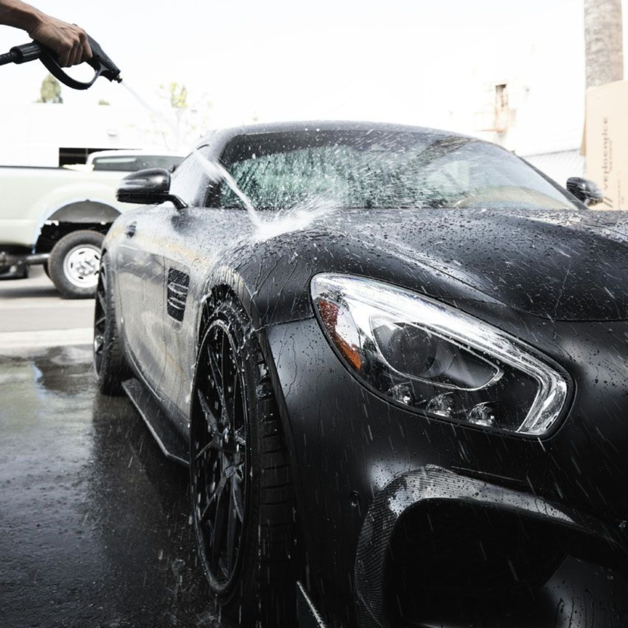Person washing a black sports car with a water hose outdoors.