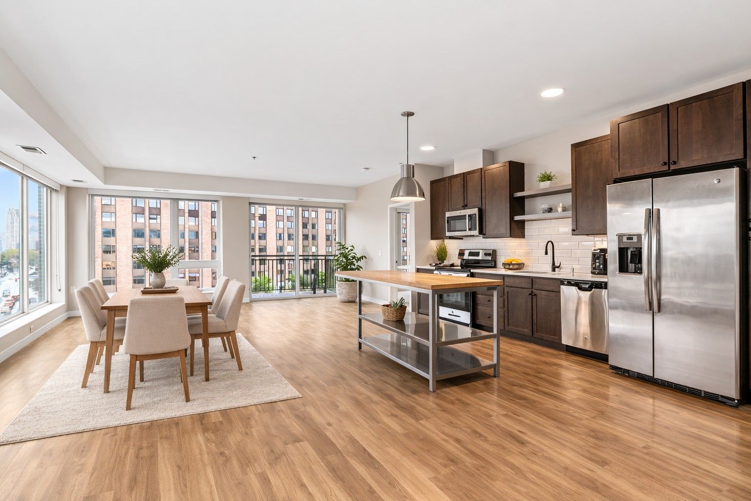 A modern open-plan kitchen here at Maverick and dining area with wooden floors, dark cabinets, a kitchen island, and a dining set.