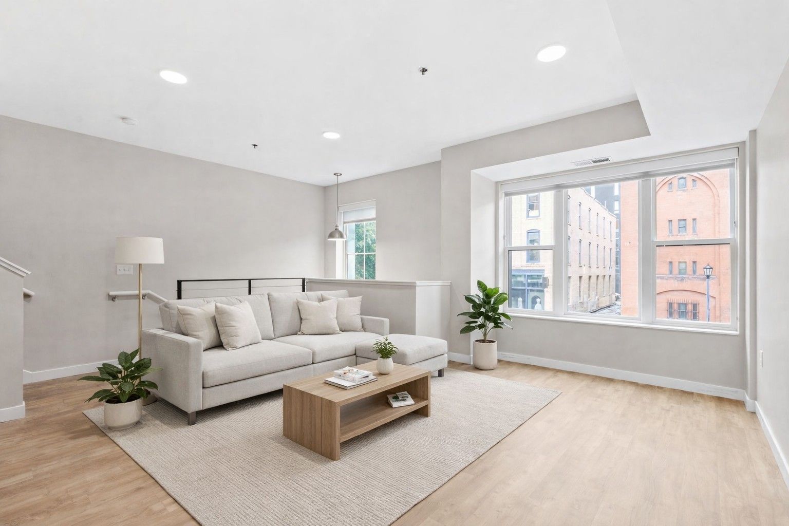 A minimalist living room here at Maverick with a light gray sectional sofa, a wooden coffee table, a floor lamp, and a large window.