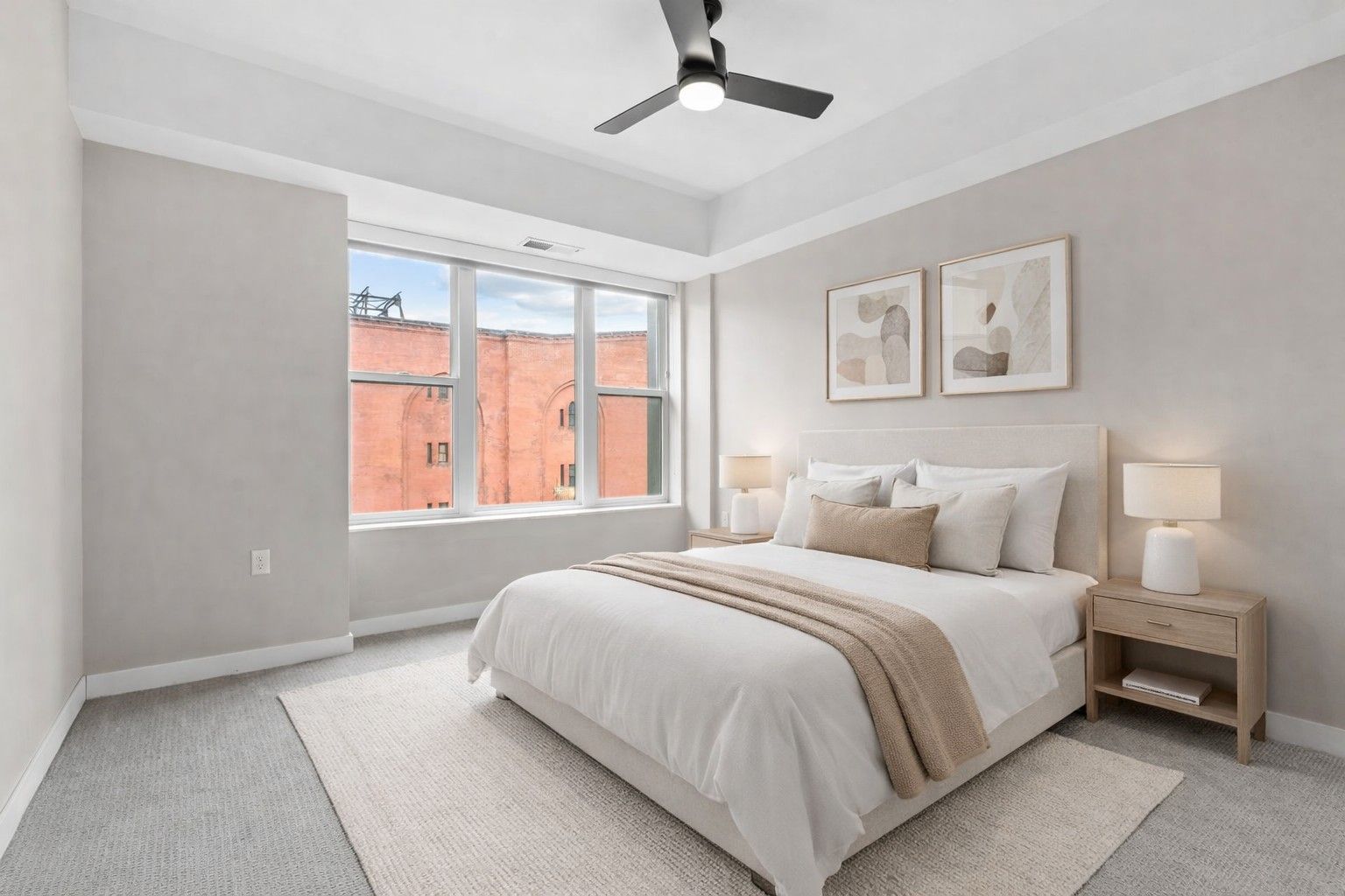 A bright, modern bedroom here at Maverick with a queen bed, two nightstands, framed wall art, gray carpet, and a ceiling fan.