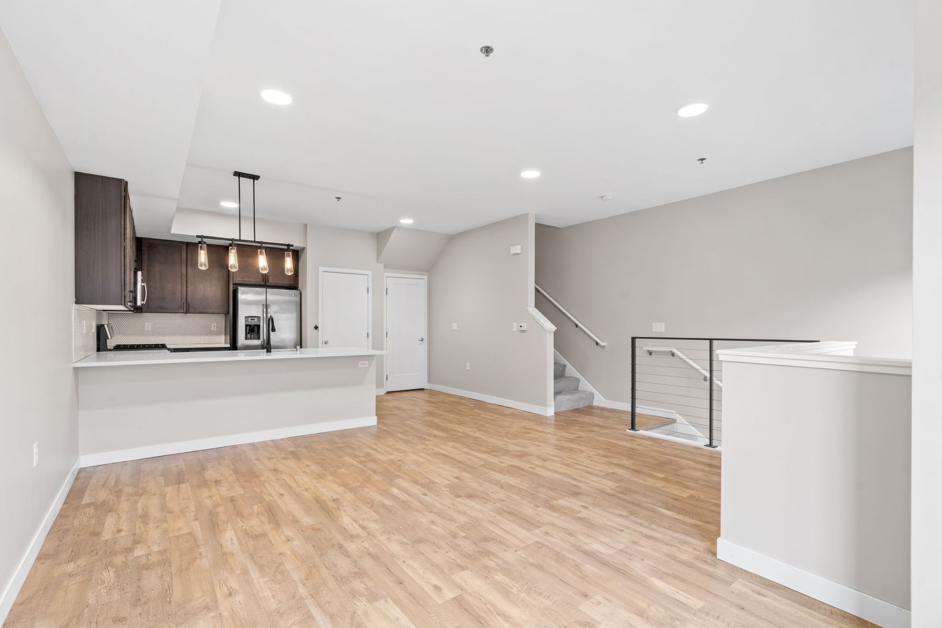 An open-concept kitchen and living area here at Maverick with wood-look flooring, light gray walls, dark cabinets, and a staircase.