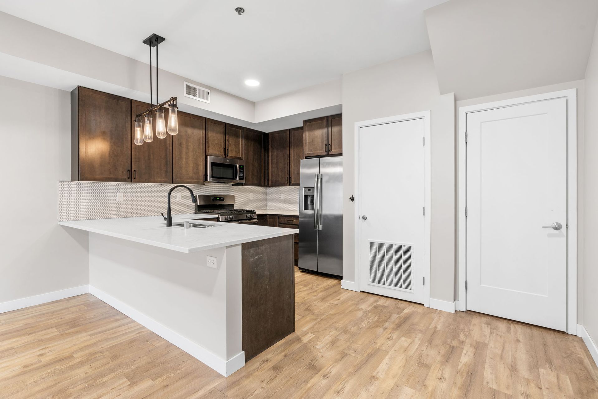A modern kitchen here at Maverick with dark brown cabinets, stainless steel appliances, a white island, and light wood flooring.
