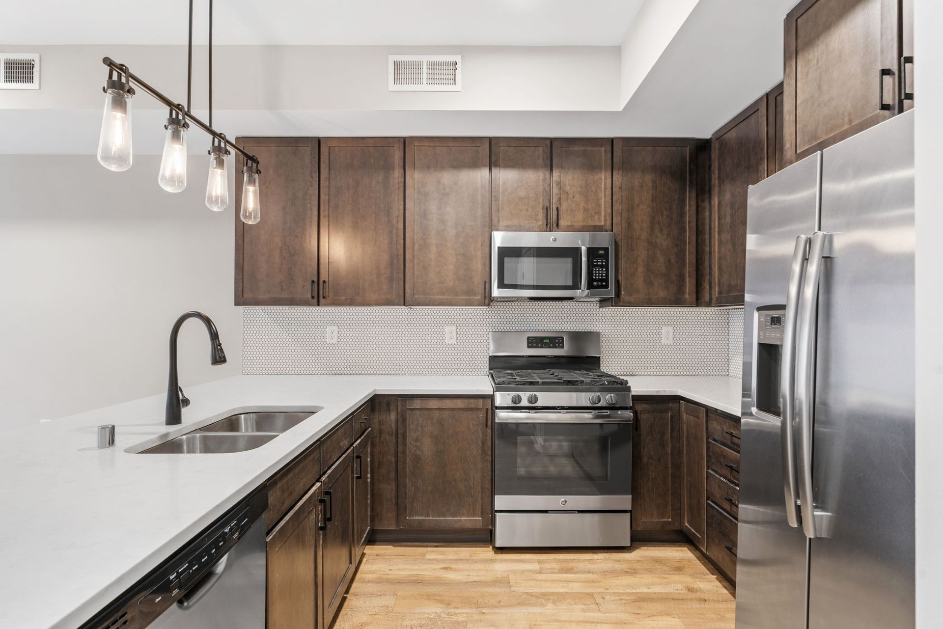 Modern kitchen with dark wood here at Maverick cabinets, stainless steel appliances, white quartz countertops, and a subway tile backsplash.