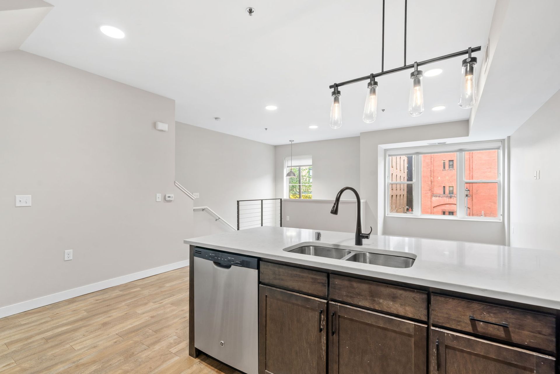 A modern kitchen island here at Maverick with a dark wood base and white countertop features a stainless dishwasher and metal faucet.