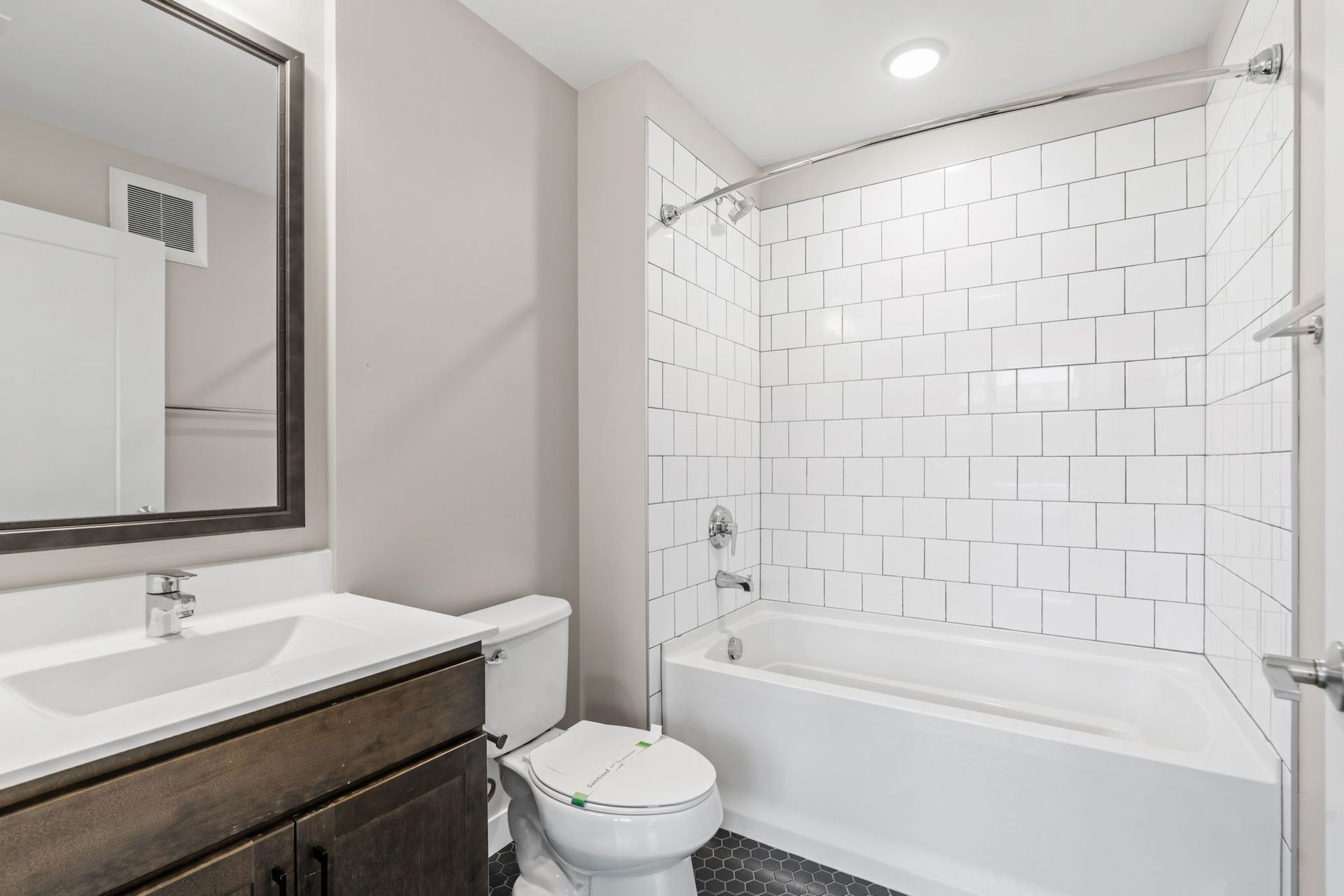 A modern bathroom with a dark wood vanity, white sink, toilet, and a bathtub with white subway tile walls.