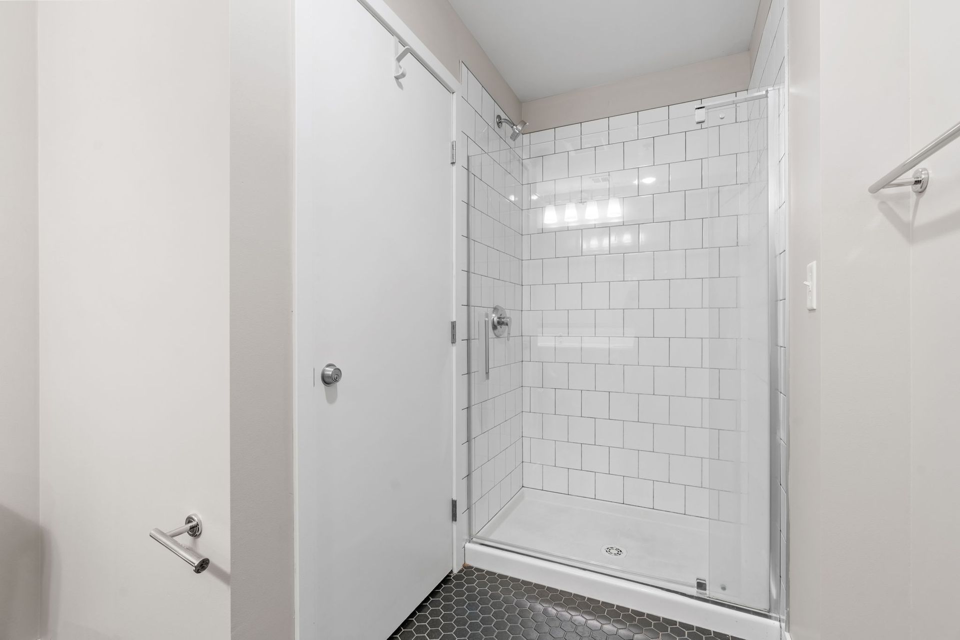 A bathroom featuring a glass-enclosed shower with white rectangular tiles in a brick pattern and a dark-tiled floor.