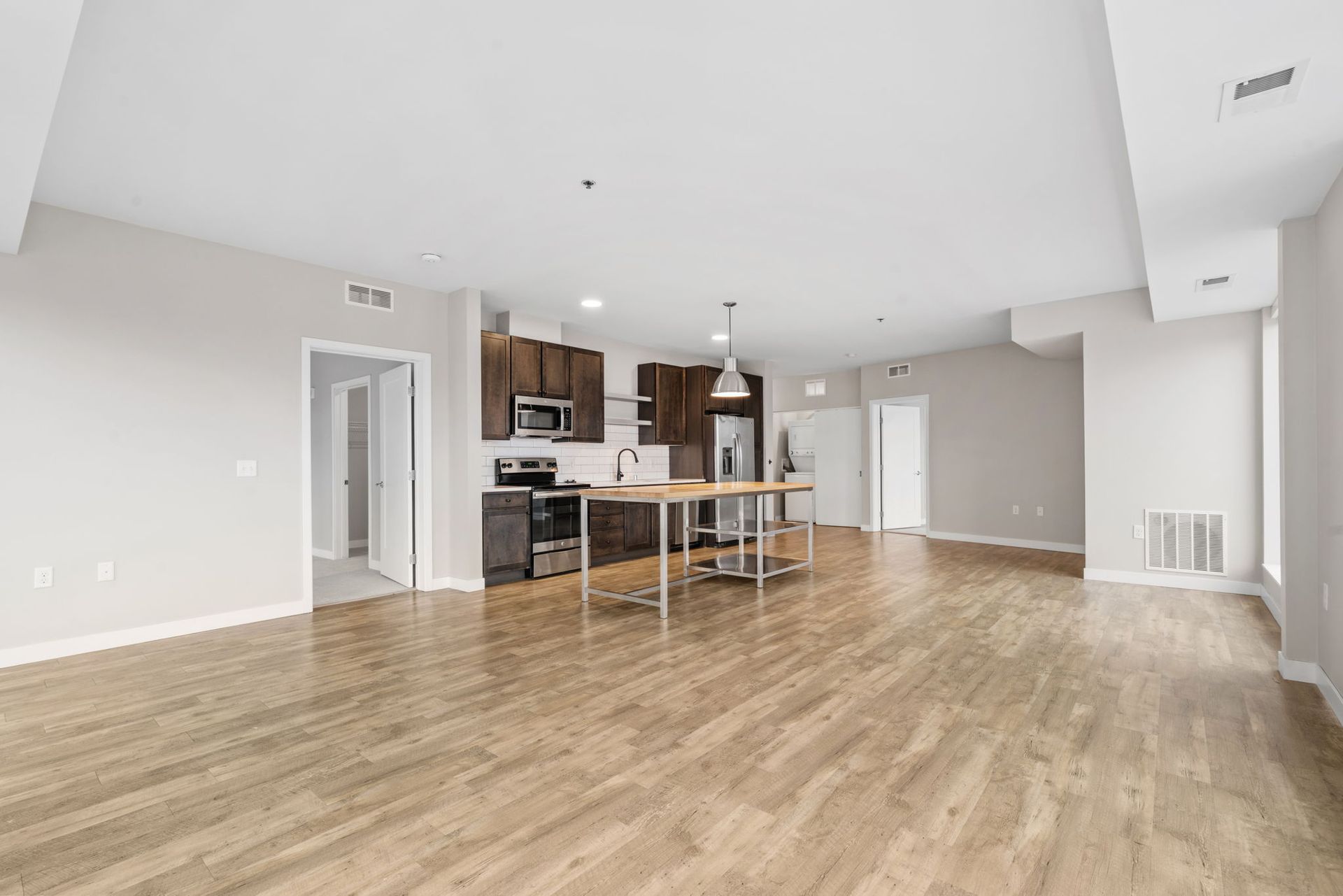An open-concept living area with light wood floors, gray walls, and a modern kitchen featuring dark brown cabinets.