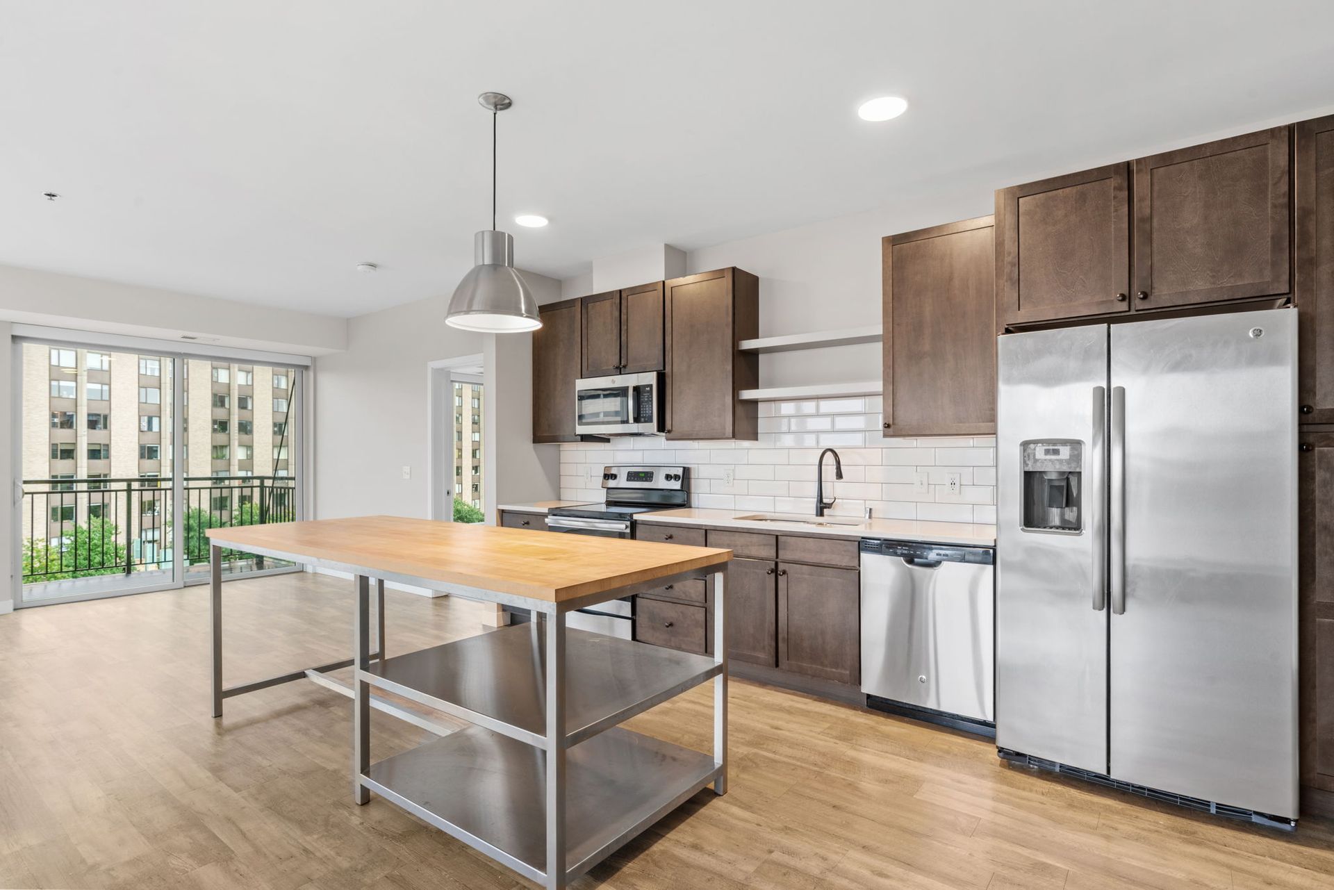 A modern kitchen with brown cabinets, stainless steel appliances, a wood-topped island, and a sliding glass door.