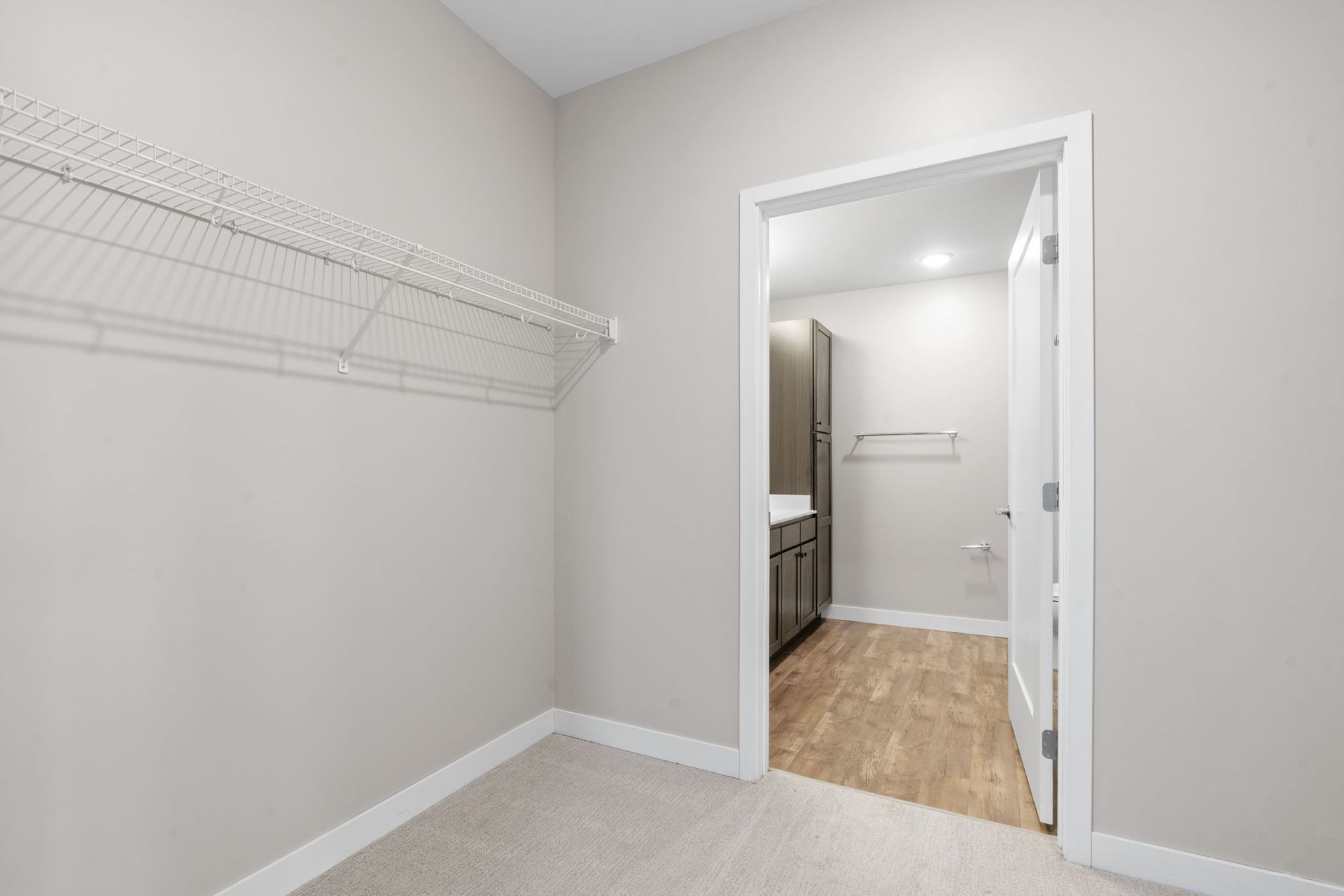 A closet with wire shelving and a doorway leading into a neutral-toned bathroom with wood-look flooring.