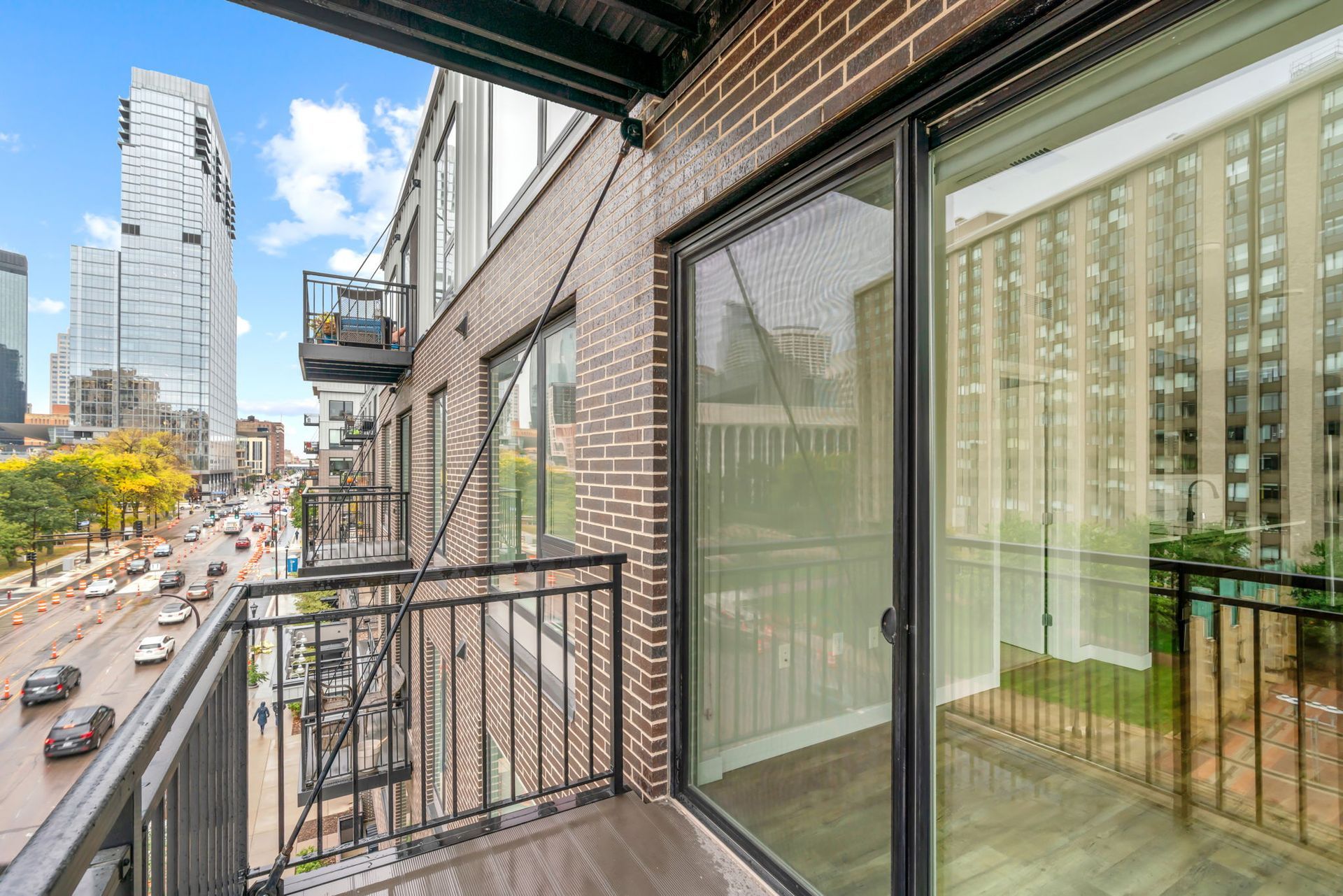 An urban balcony overlooks a city street with tall buildings on a bright, cloudy day.