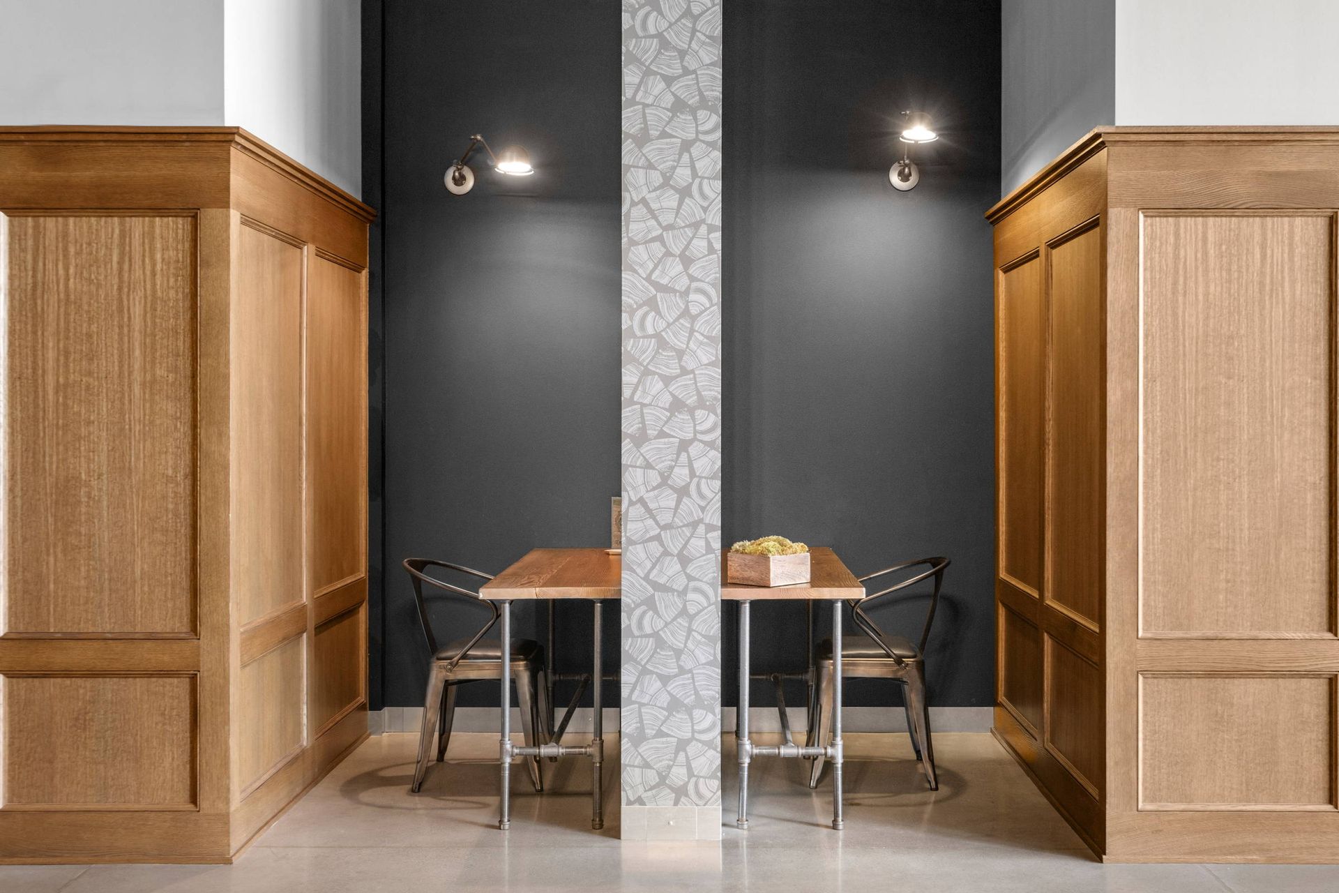 Two wooden-paneled booths face opposite sides of a central patterned pillar, each with a wooden table and metal chairs.