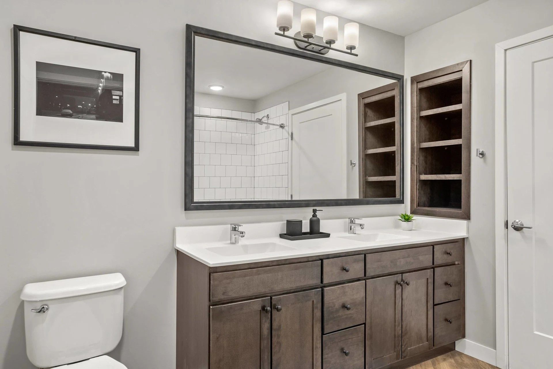 Modern bathroom here at Maverick featuring a double-sink vanity with dark wood cabinets, a large mirror, and open wall shelving.