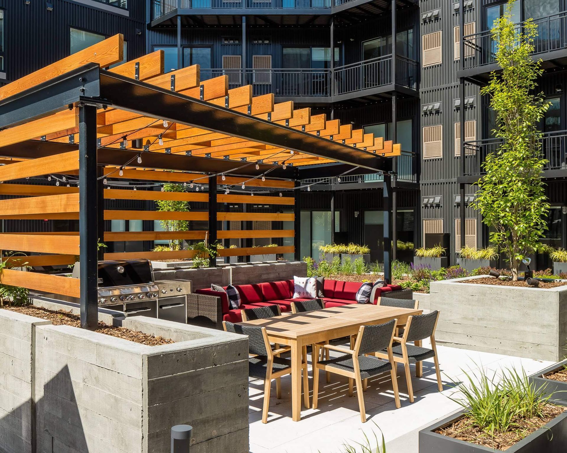 A patio with a table and chairs under a pergola in front of a building.