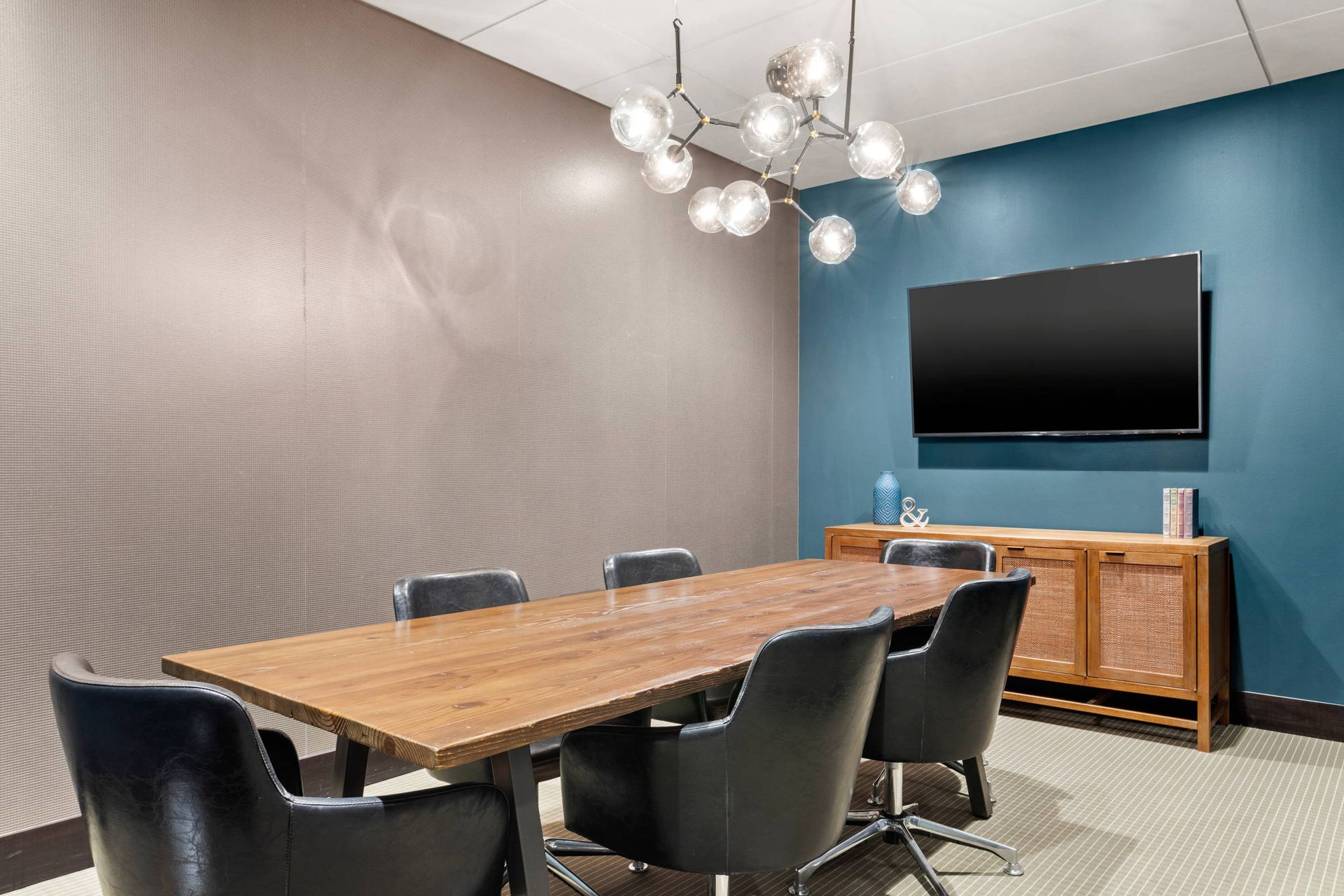 A conference room with a long wooden table and chairs and a flat screen tv.