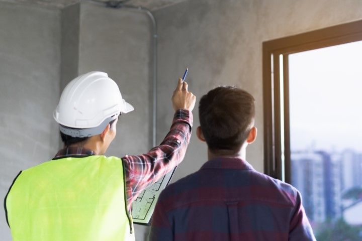 Two men wearing hard hats discuss renovation plans next to a window