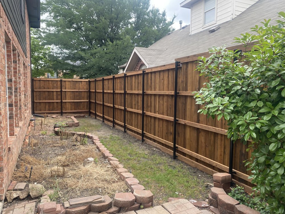 Wooden fence along a brick house and yard with a small garden area.