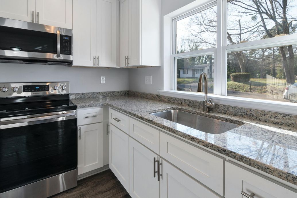 White kitchen with stainless steel appliances, granite countertops, and a window overlooking a yard.