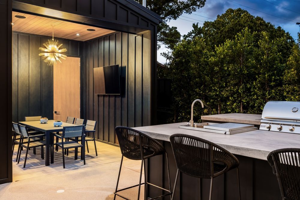 Outdoor kitchen and dining area with a grill, sink, bar stools, and a table with chairs.