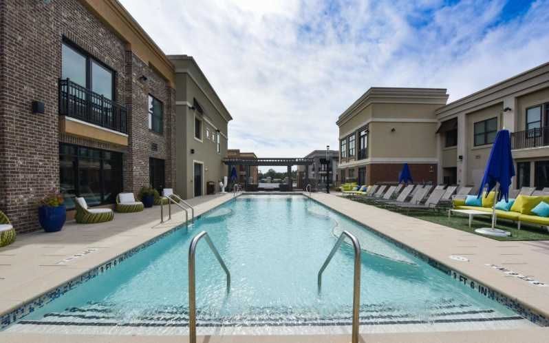 Pool between buildings with lounge chairs; sunny, blue sky.