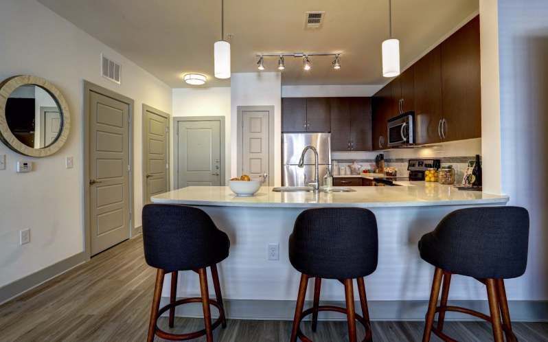 Modern kitchen with island and bar stools. Dark cabinets, stainless steel appliances.