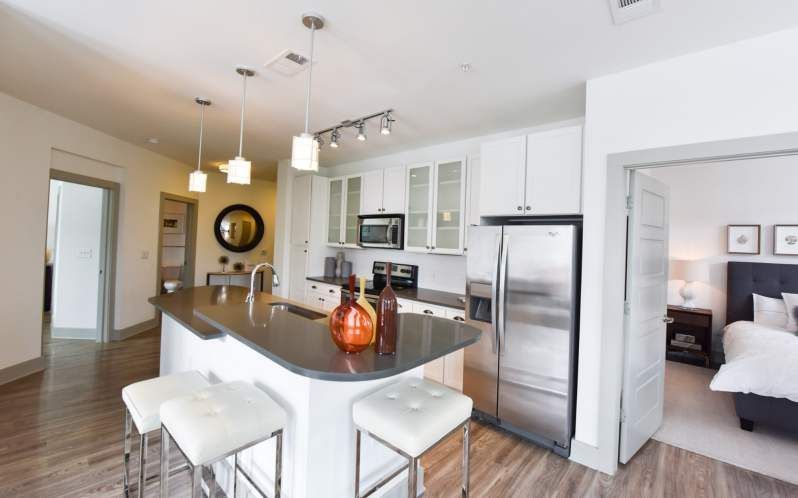 Modern kitchen with island, stainless steel appliances, and a view into a bedroom.