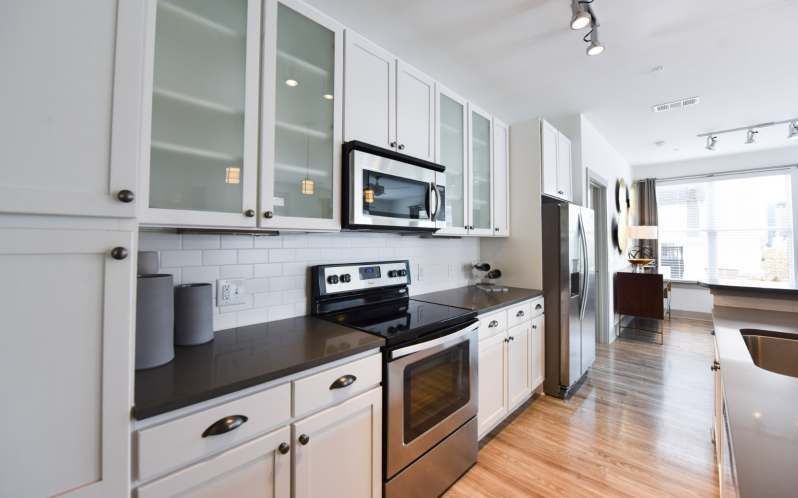 White kitchen with stainless steel appliances, dark countertops, and cabinets.