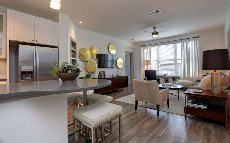 Modern apartment living room with kitchen island and seating, stainless steel appliances, and neutral color palette.
