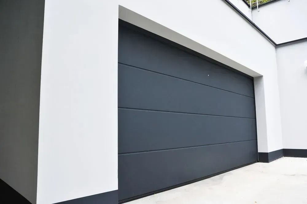 A Black Garage Door Is Sitting on The Side of A White Building — Lock & Door in Wodonga, VIC