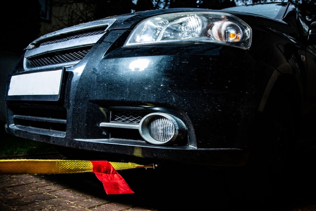 A black car is parked on the side of the road next to a yellow tape.