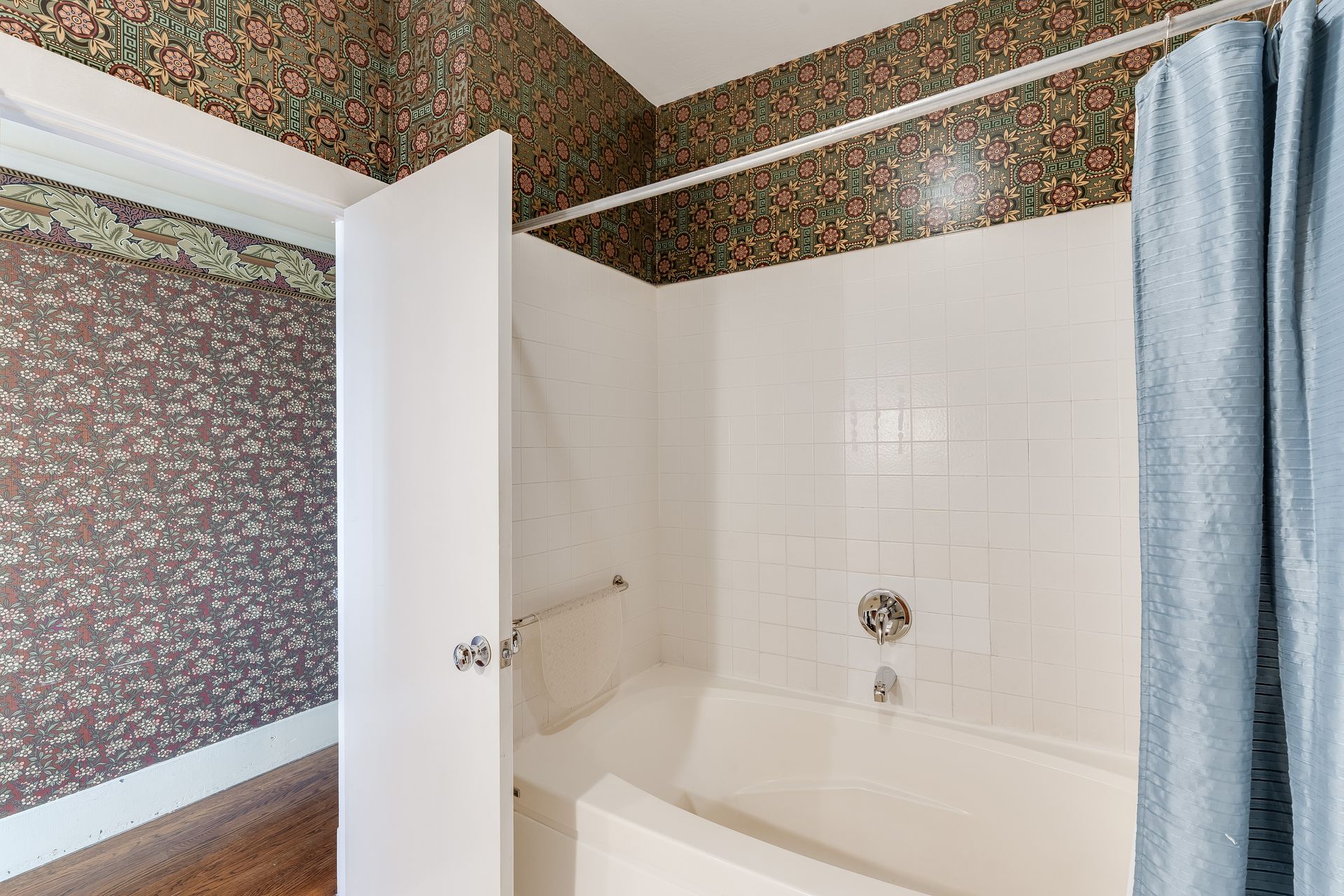 Bathroom with floral wallpaper, white tub, and blue shower curtain.