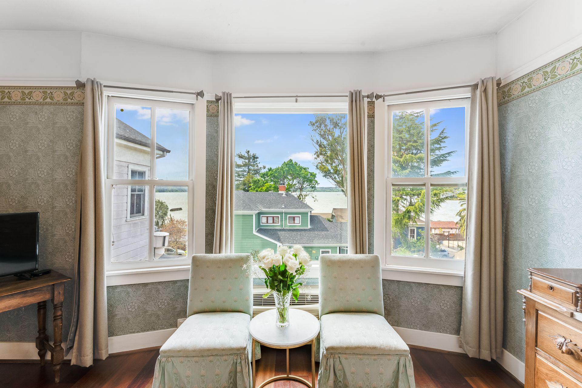Charming room with curved windows, two chairs facing outside view, and a small table with flowers.
