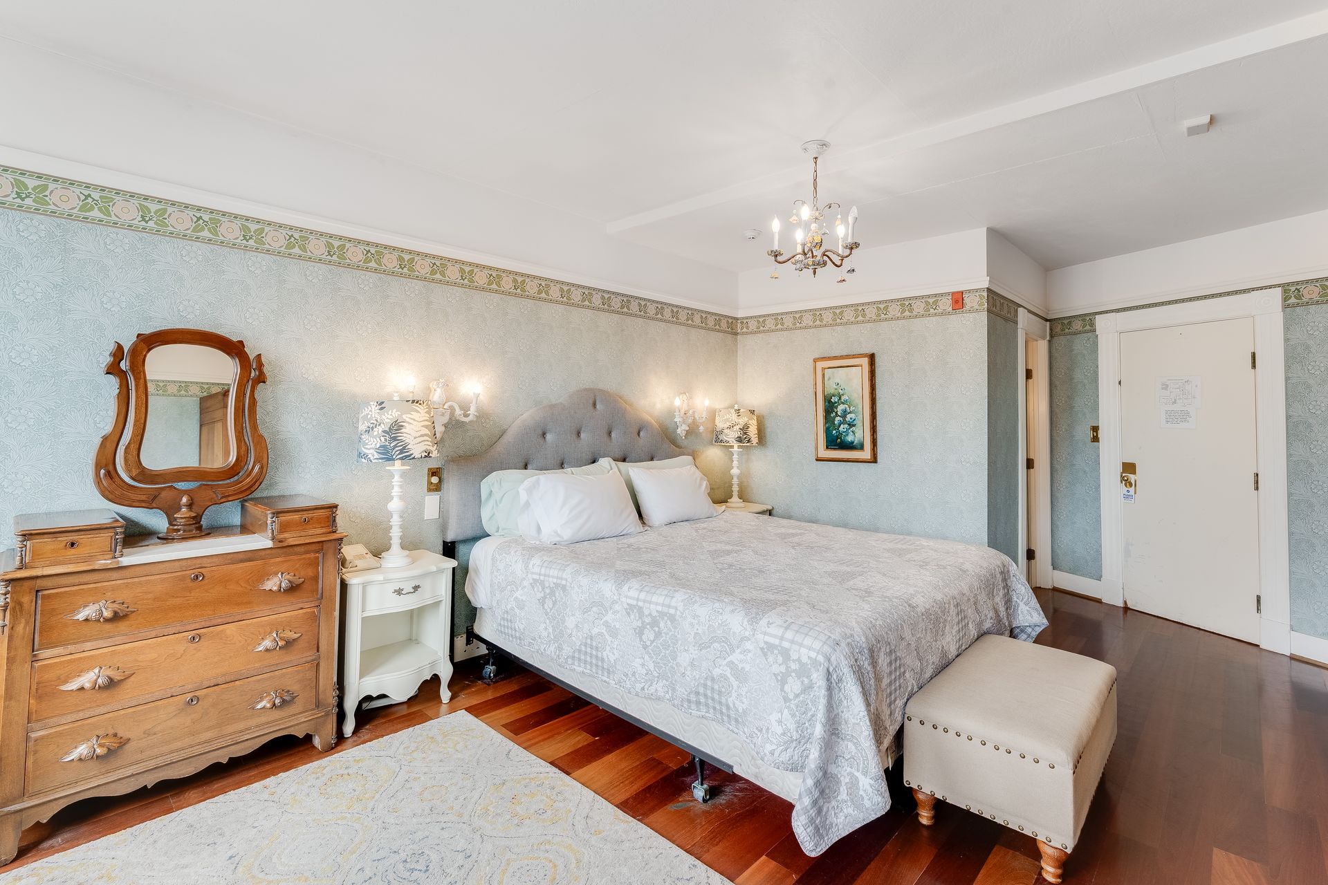 Bedroom with a bed, dresser, mirror, and nightstand. Soft colors, hardwood floors.
